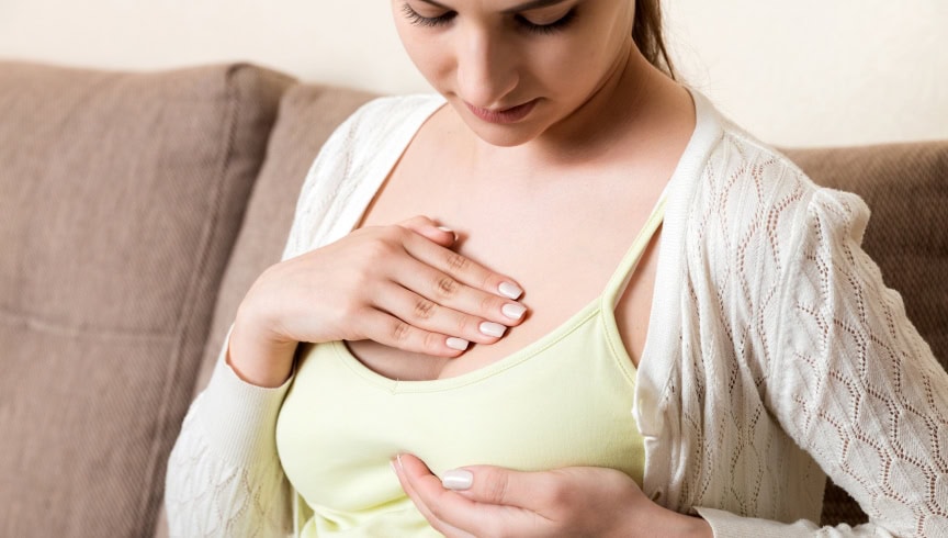 Una mujer con una mano en el pecho, y otra debajo de su pezon, preocupada por síntomas de posibles problemas de salud.